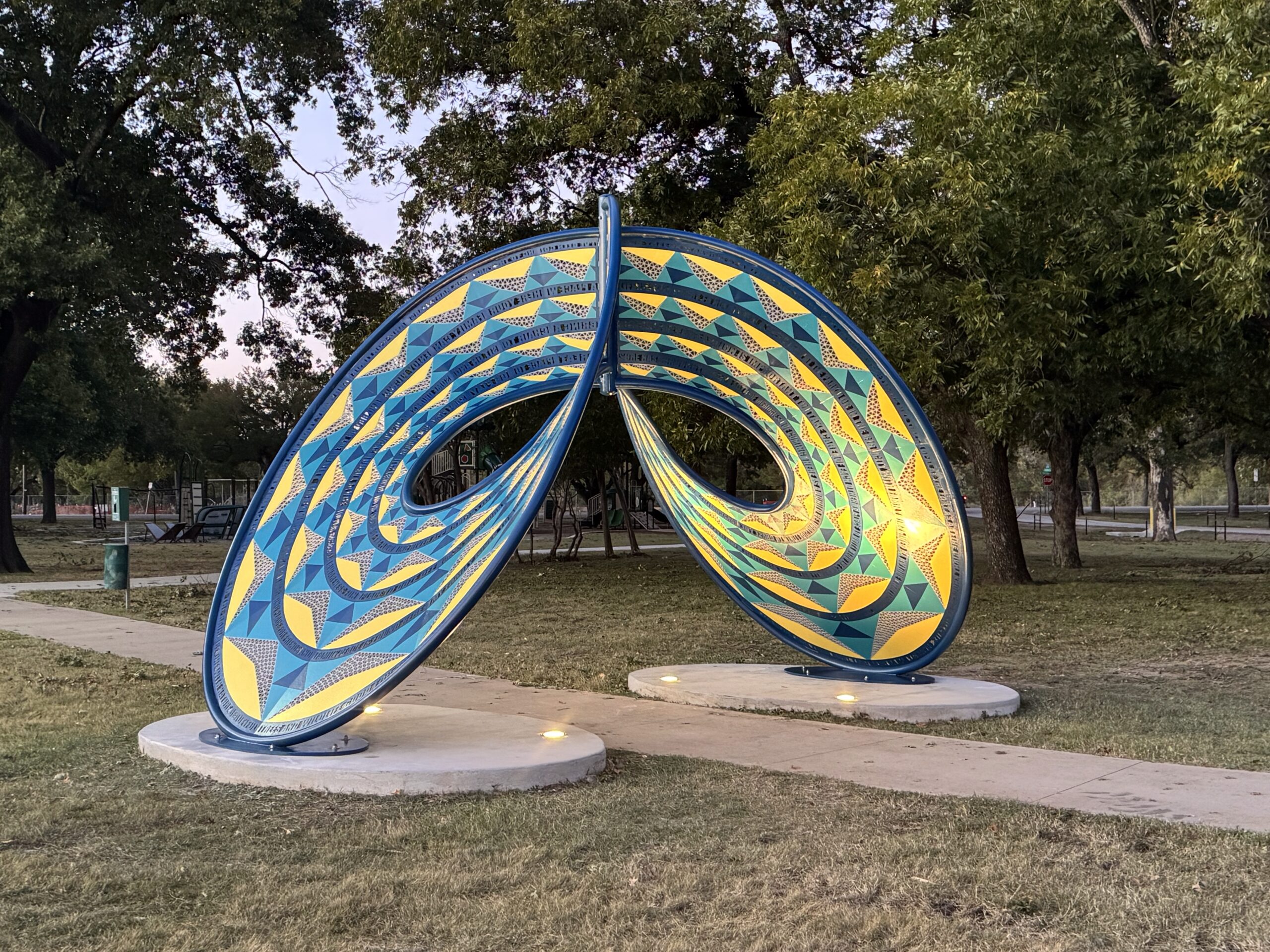 “Energetic” sculpture by artist Blessing Hancock in Fort Worth’s Sycamore Park — a colorful, figure-eight-shaped metal artwork with curving forms and community-inspired text bands, fabricated and installed by Gizmo Art Production.