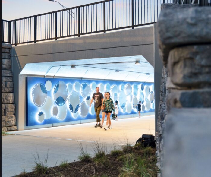 “Petal–Drop–Flutter” by Blessing Hancock — a tunnel installation of sculptural metal panels shaped like petals and droplets, illuminated by color-changing LEDs, fabricated and installed by Gizmo Art Production in Lexington, Kentucky.