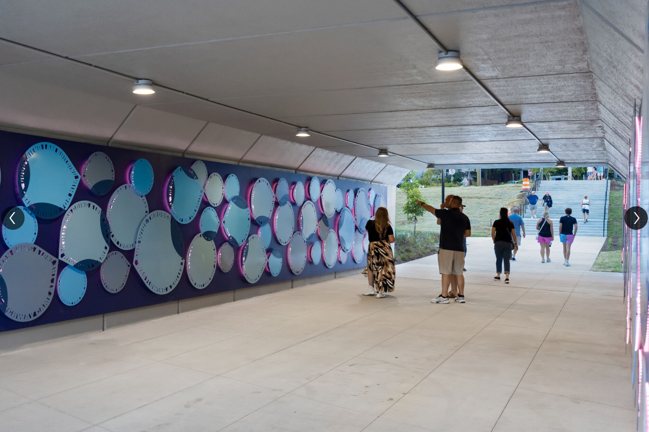 “Petal–Drop–Flutter” by Blessing Hancock — a tunnel installation of sculptural metal panels shaped like petals and droplets, illuminated by color-changing LEDs, fabricated and installed by Gizmo Art Production in Lexington, Kentucky.